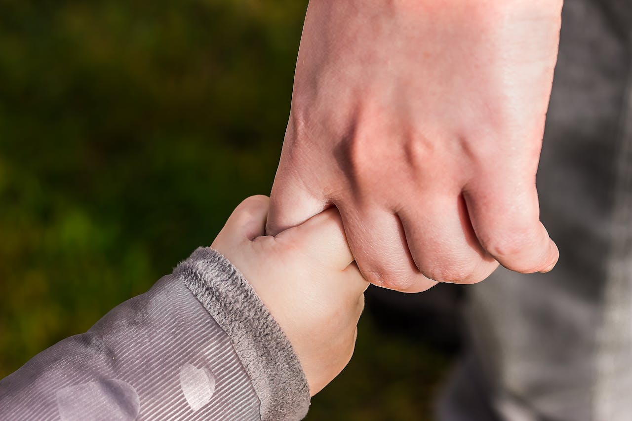 services-07 A close-up of a child and parent holding hands in a park, symbolizing love and trust.