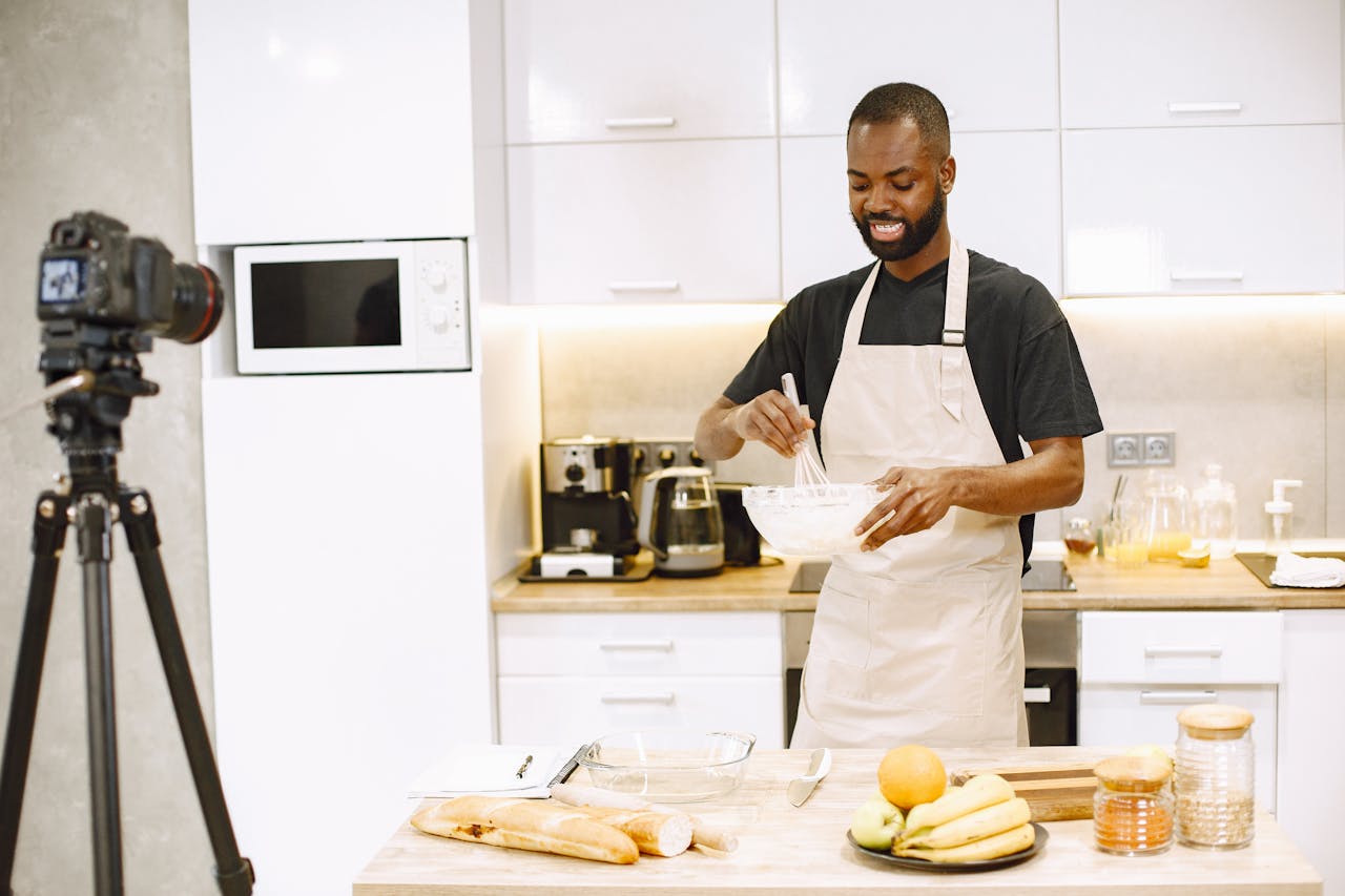 African American man cooking in kitchen for a vlogging session, recorded with DSLR camera.